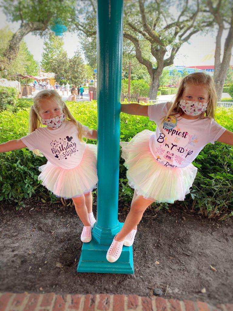 Birthday squad shirts on with matching Disney masks as two girls lean off a lightpost. 