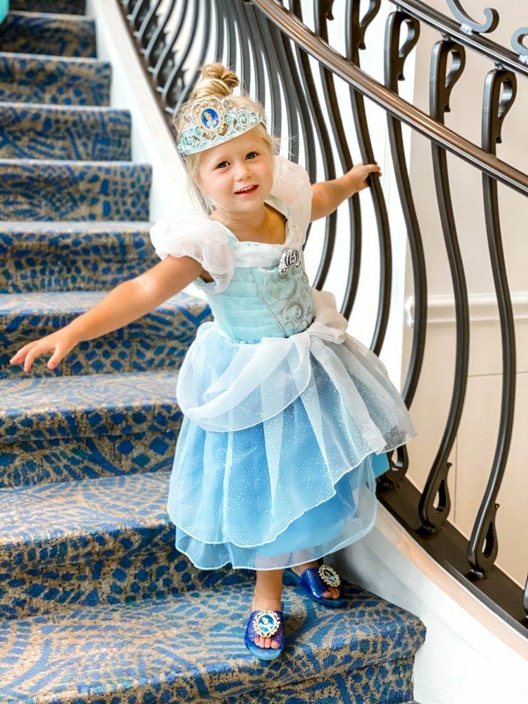 Little girl leaning from the staircase banister dressed as Cinderella.