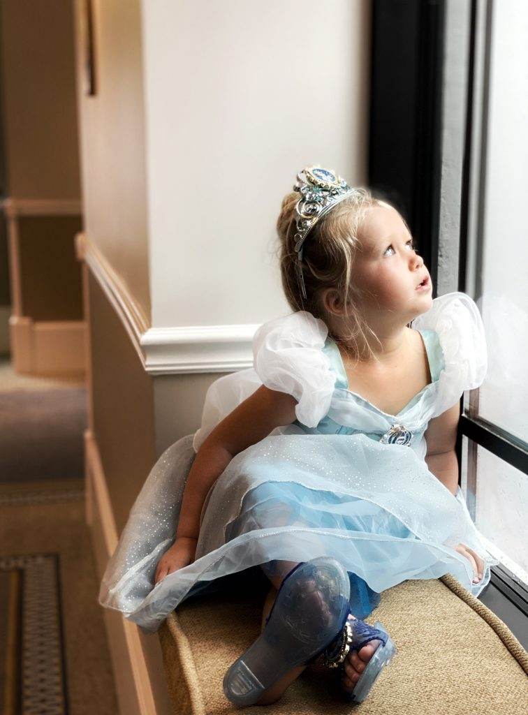 Young girl dressed as Cinderella looks out a window